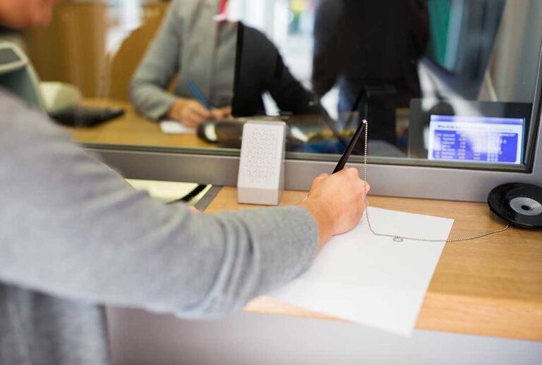 A person checks their phone and laptop while reviewing digital bank account statements at home.